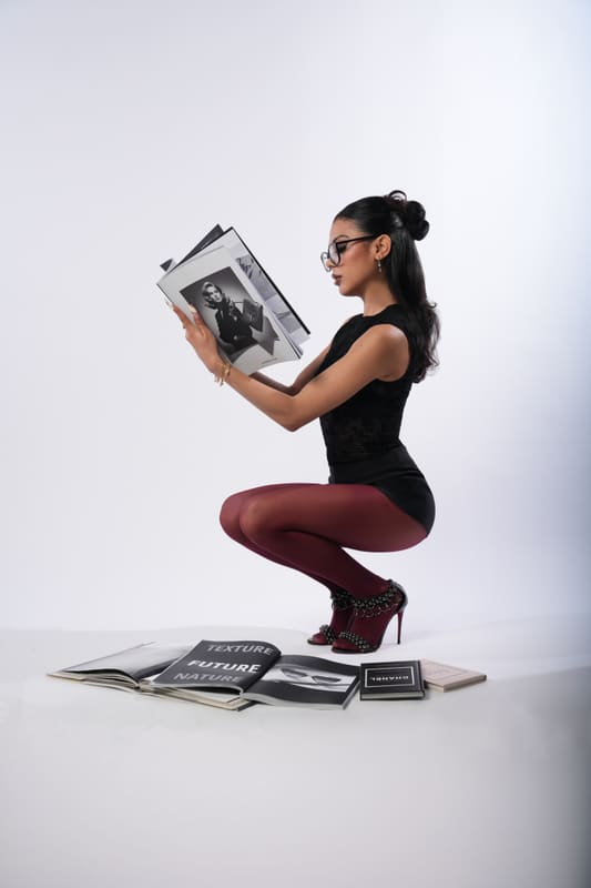 Crouching in a black top and burgundy tights, reading a magazine