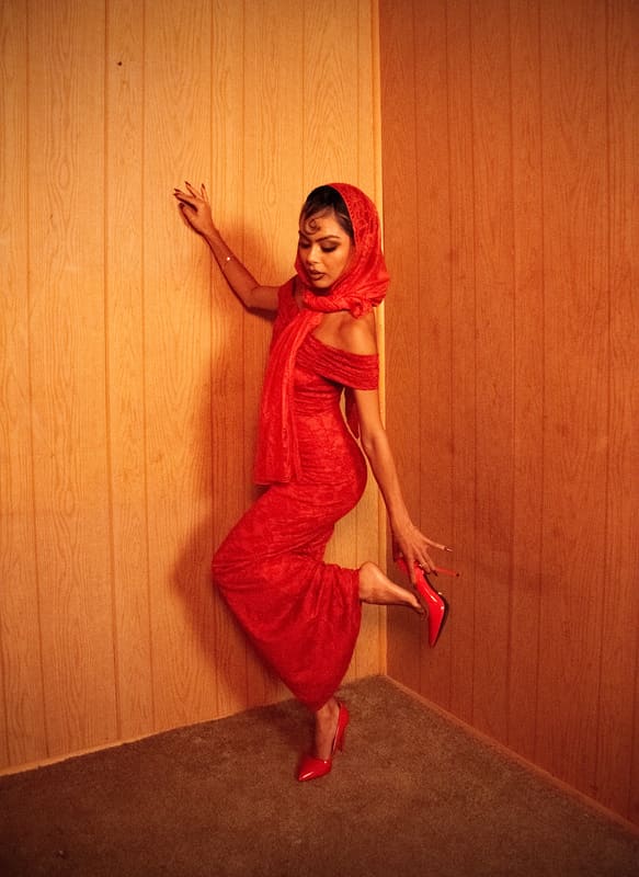 Leaning against a wood-panelled wall in a red lace dress