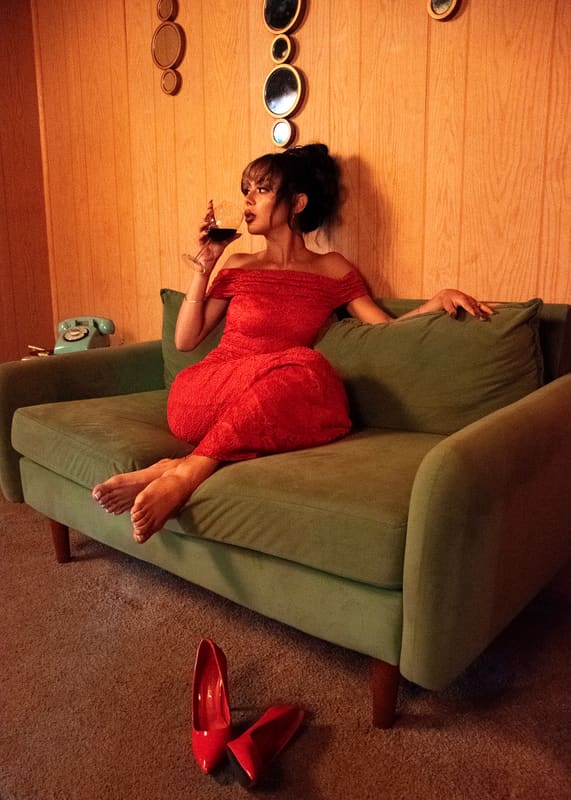 Seated on a green sofa in a red dress, holding a vintage telephone