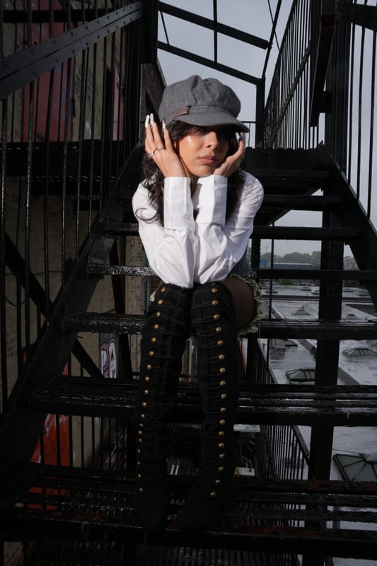 Seated on a fire escape in a newsboy cap, black and white